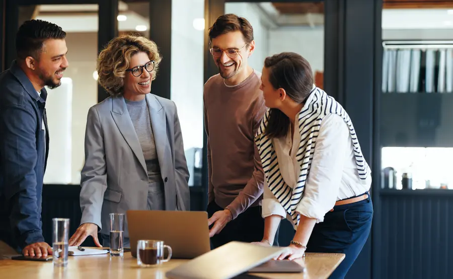 Eine diverse Gruppe von Führungskräften und Mitarbeitenden steht um einen Tisch in einem modernen Büro und diskutiert gemeinsam vor einem Laptop – symbolische Darstellung für Zusammenarbeit, Leadership-Entwicklung und Führungskräfte Coaching im Unternehmenskontext.